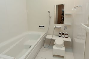 A modern bathroom with a bathtub, a shower, a toilet, and a shelf with toiletries. - Sumidanagaya - Hostel (Tokyo)