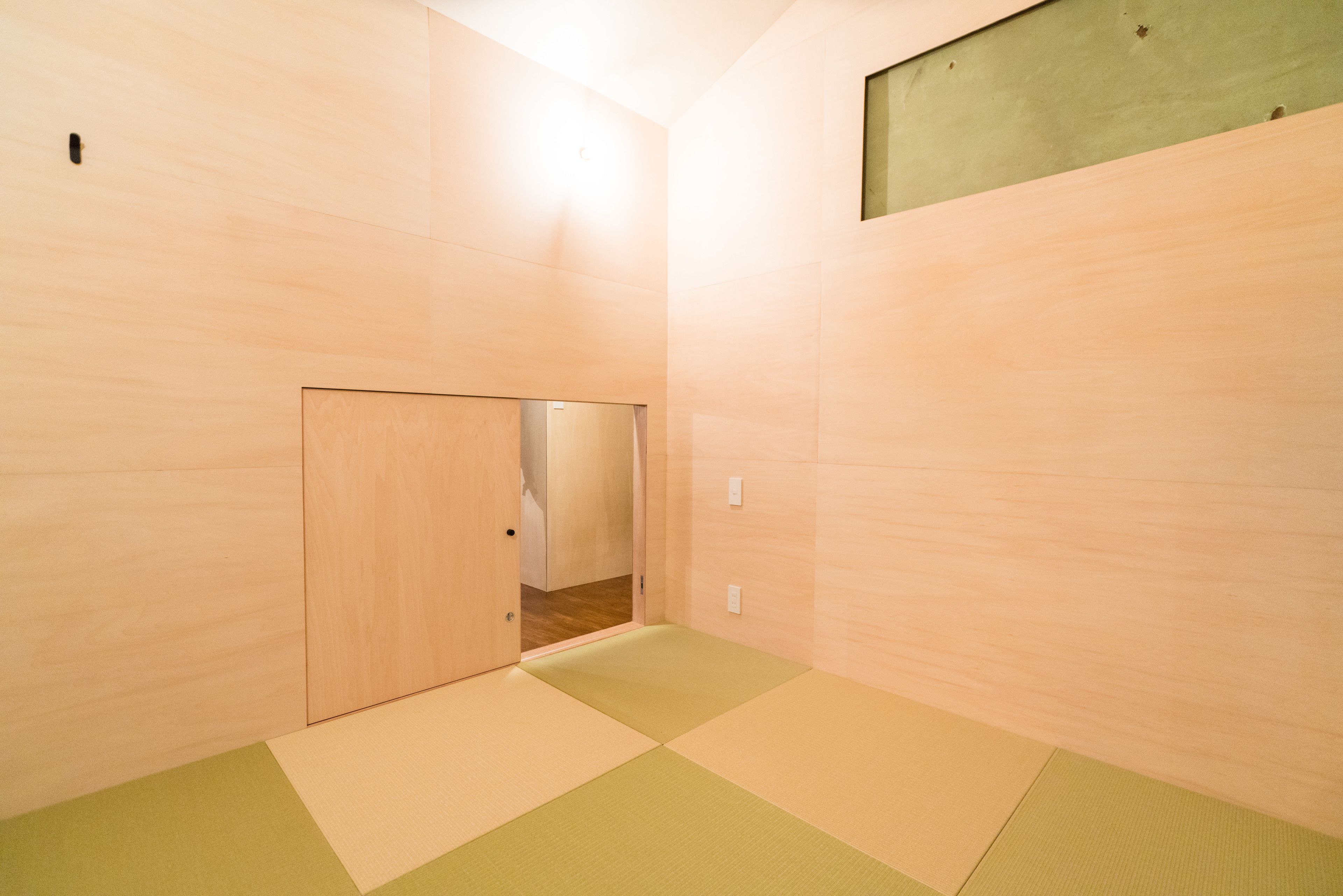 Ein Zimmer mit Holzwänden und einem Boden aus grün-beigem Tatami-Bodenbelag.