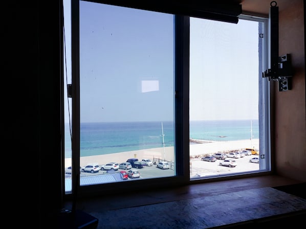 A view from a room with a large window overlooking a beach and a parking lot.