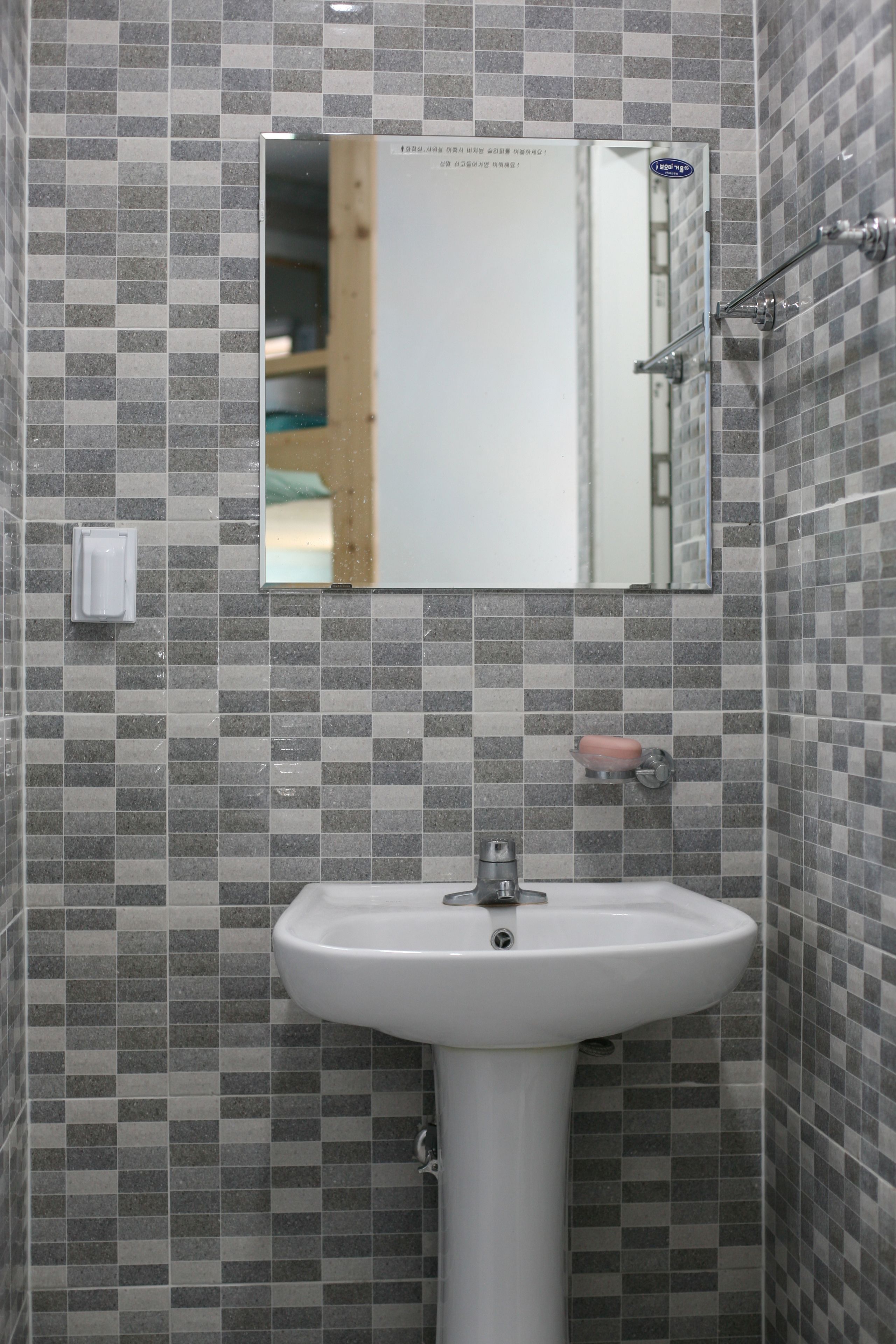 Un baño con lavamanos blanco, espejo y paredes con azulejos.