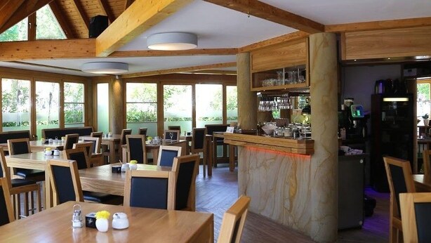A restaurant with wooden tables and chairs, large windows, and a bar area. - Hotel Zwei Länder (Apolda)