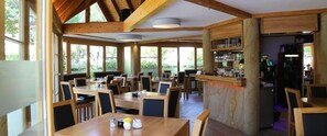 A restaurant with wooden tables and chairs, large windows, and a bar area. - Hotel Zwei Länder (Apolda)