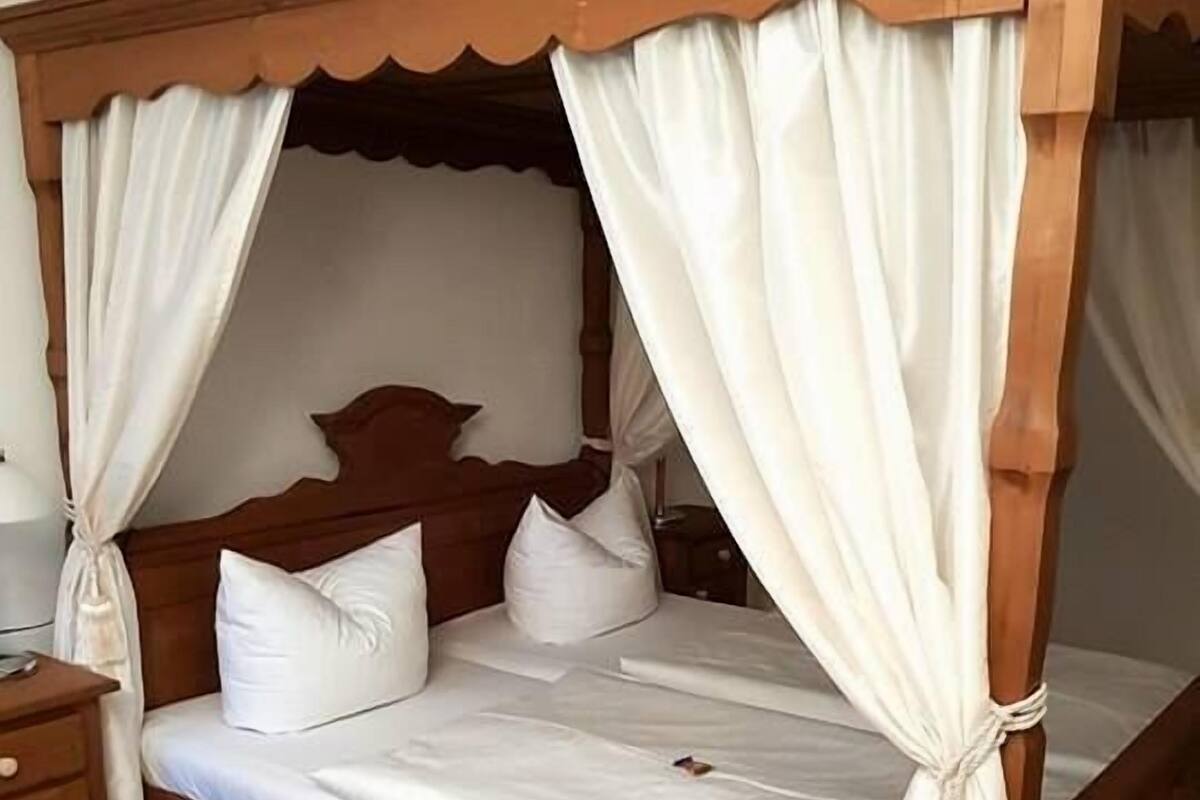 A four-poster bed with white linens and a wooden frame, a bedside table, and a patterned rug.