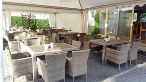 An outdoor seating area with wicker furniture and tables, covered by a canopy. - Hotel Zwei Länder (Apolda)