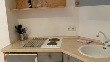 A compact kitchen with a built-in stove, a sink, and a wooden shelf above the counter.