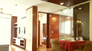 A modern hotel room with a wooden floor, a dining area with a red tablecloth, and a large sliding glass door leading to a balcony. - Henry Apt Expo Secc Goft SWPool F11th (Ho Chi Minh City)