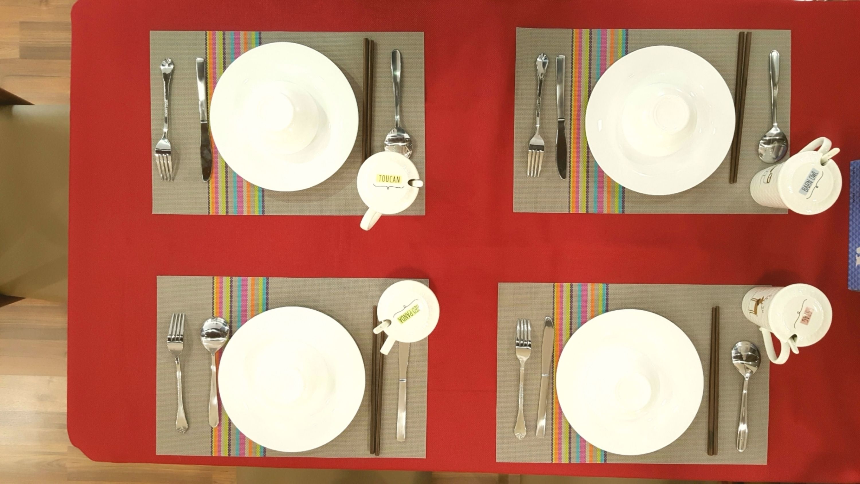 Una mesa de comedor dispuesta con cuatro platos, cubiertos y un porta servilletas.
