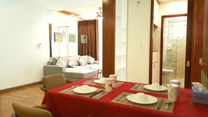 A dining area with a red table set for four, a sofa in the background, and a view of a bathroom with a shower and toilet.