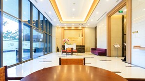 Eine großzügige Lobby mit einem großen Holztisch, einer Rezeption und einem violetten Sofa.