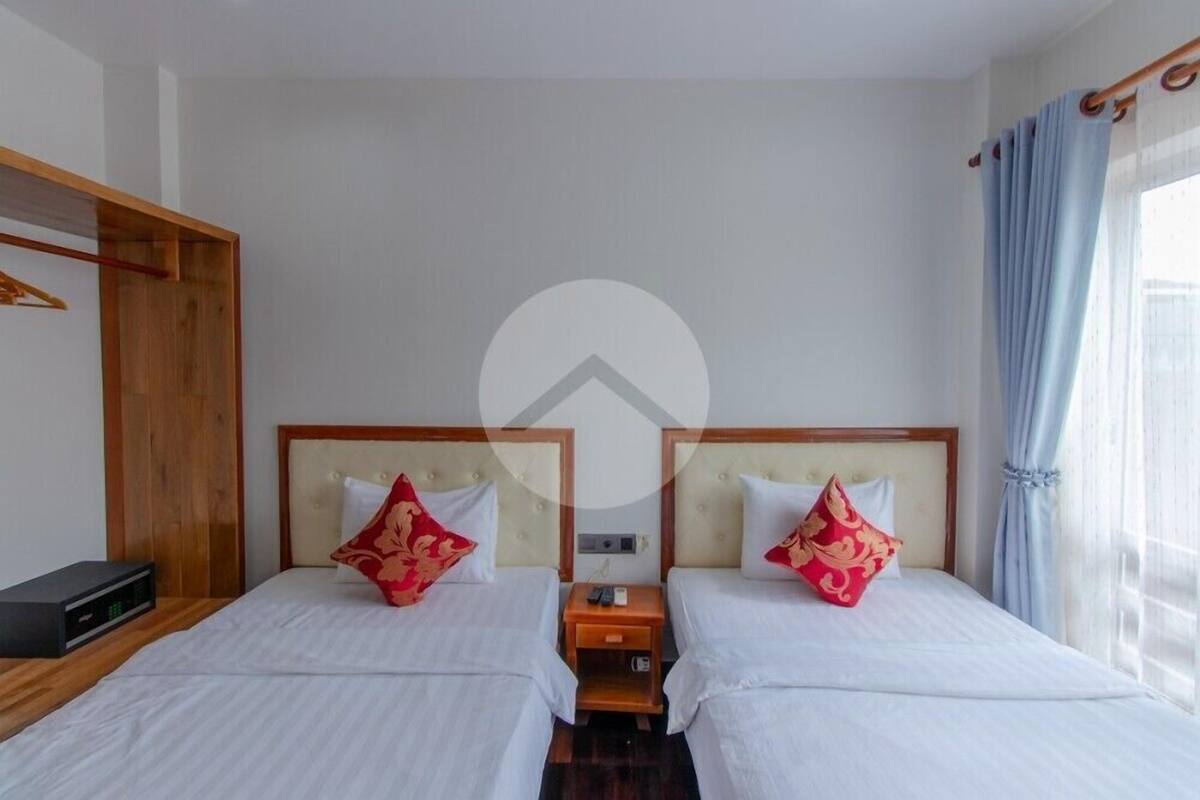 A hotel room with two beds, each with a wooden headboard and white bedding. There is a wooden nightstand between the beds with a remote control and a small table.