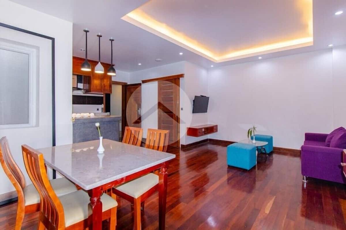 A modern living room with a dining area, wooden flooring, and a kitchen in the background.