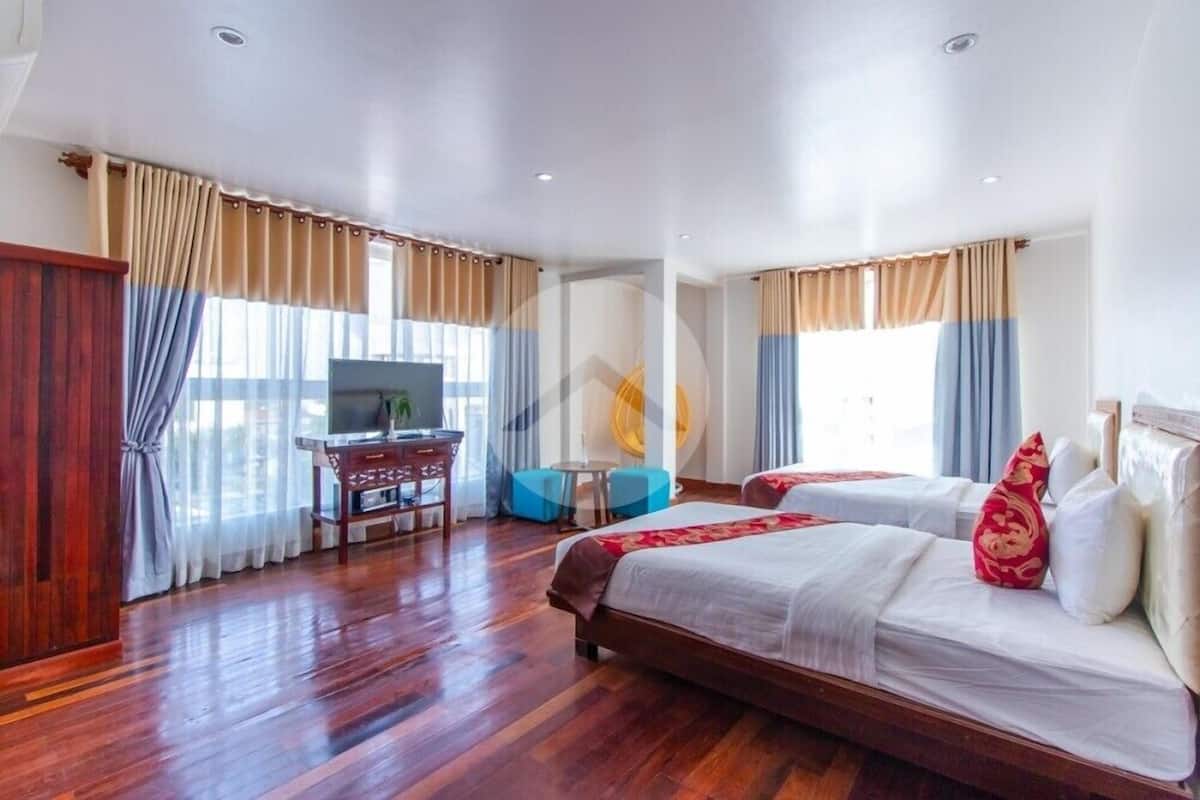 A hotel room with two beds, a desk with a chair, a TV, and a small table with a chair.