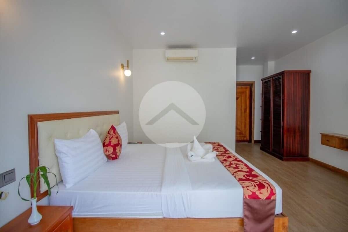 A hotel room with a bed, a nightstand with a vase, a wardrobe, and a door leading to another room.