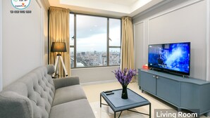 Un salon comprenant un canapé, une table basse, un téléviseur et offrant une vue sur le paysage urbain grâce à de grandes fenêtres.