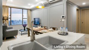 Un salon et une salle à manger modernes, dotés d’une grande fenêtre, d’un téléviseur à écran plat, d’une table à manger et d’un coin cuisine avec un évier.