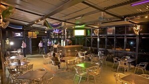 An outdoor dining area with metal tables and chairs, a bar area, and large windows. - Ivys Hotel (Kampala)