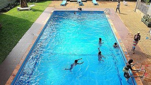 A rectangular swimming pool with clear blue water, surrounded by a tiled deck and a grassy area. - Ivys Hotel (Kampala)