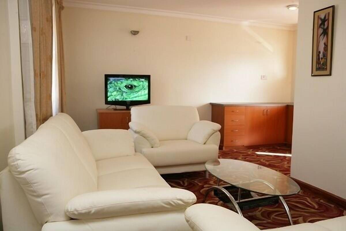 A living room with a sofa, armchair, and a glass coffee table. A television is on a stand in the background.
