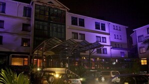 A multi-story hotel with a covered entrance and several vehicles parked in front. - Ivys Hotel (Kampala)