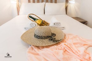 A neatly made bed with a bottle of champagne, a straw hat, and rolled towels.
