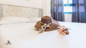 A neatly made bed with white linens, a brown hat with a bow, and a pink flower on the bed in a hotel room.