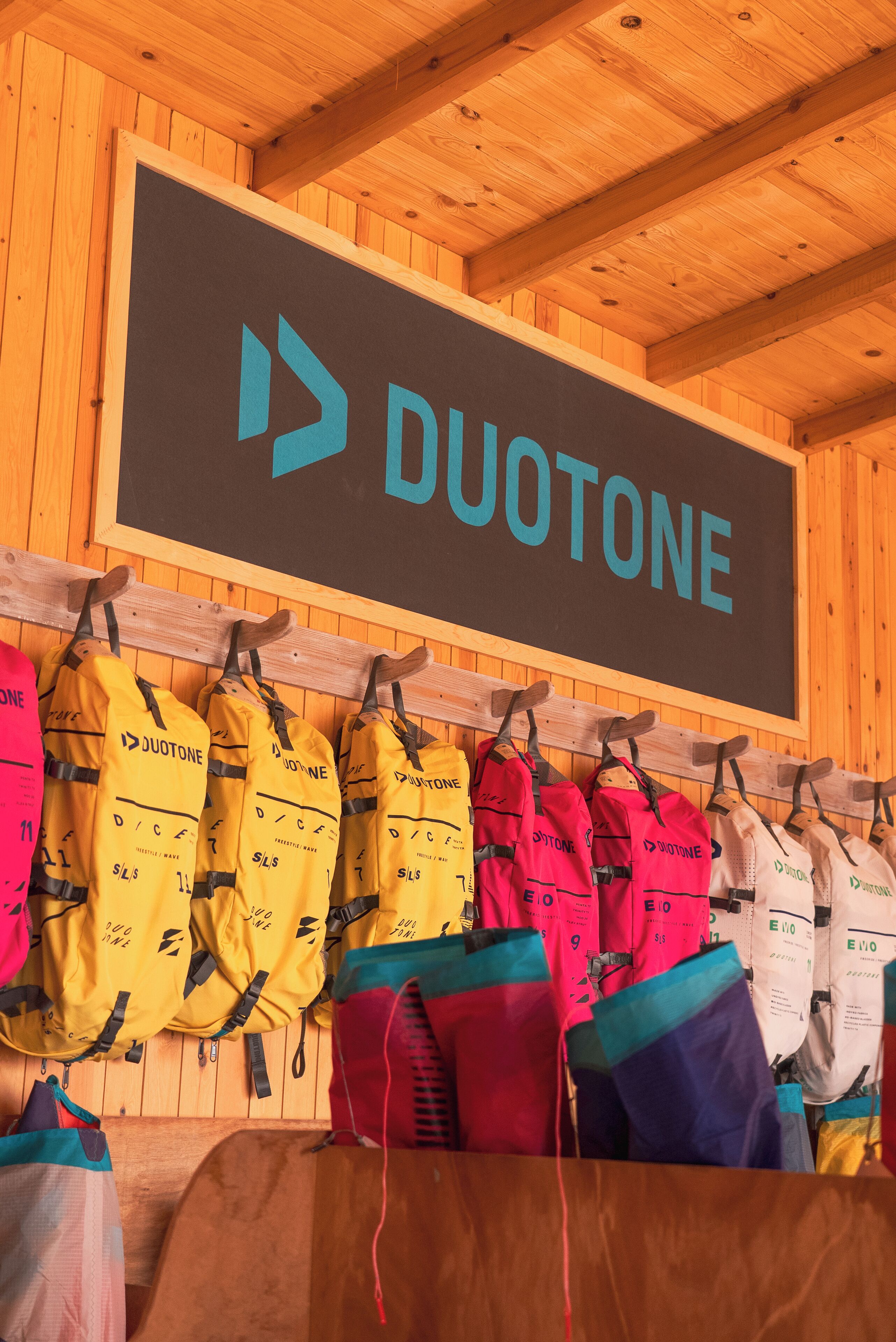 Interior de madera con un cartel que dice "DUOTONE" y varias bolsas colgadas en un perchero.