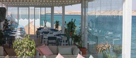 Terraza con asientos y mesas con vistas a una playa y al mar.