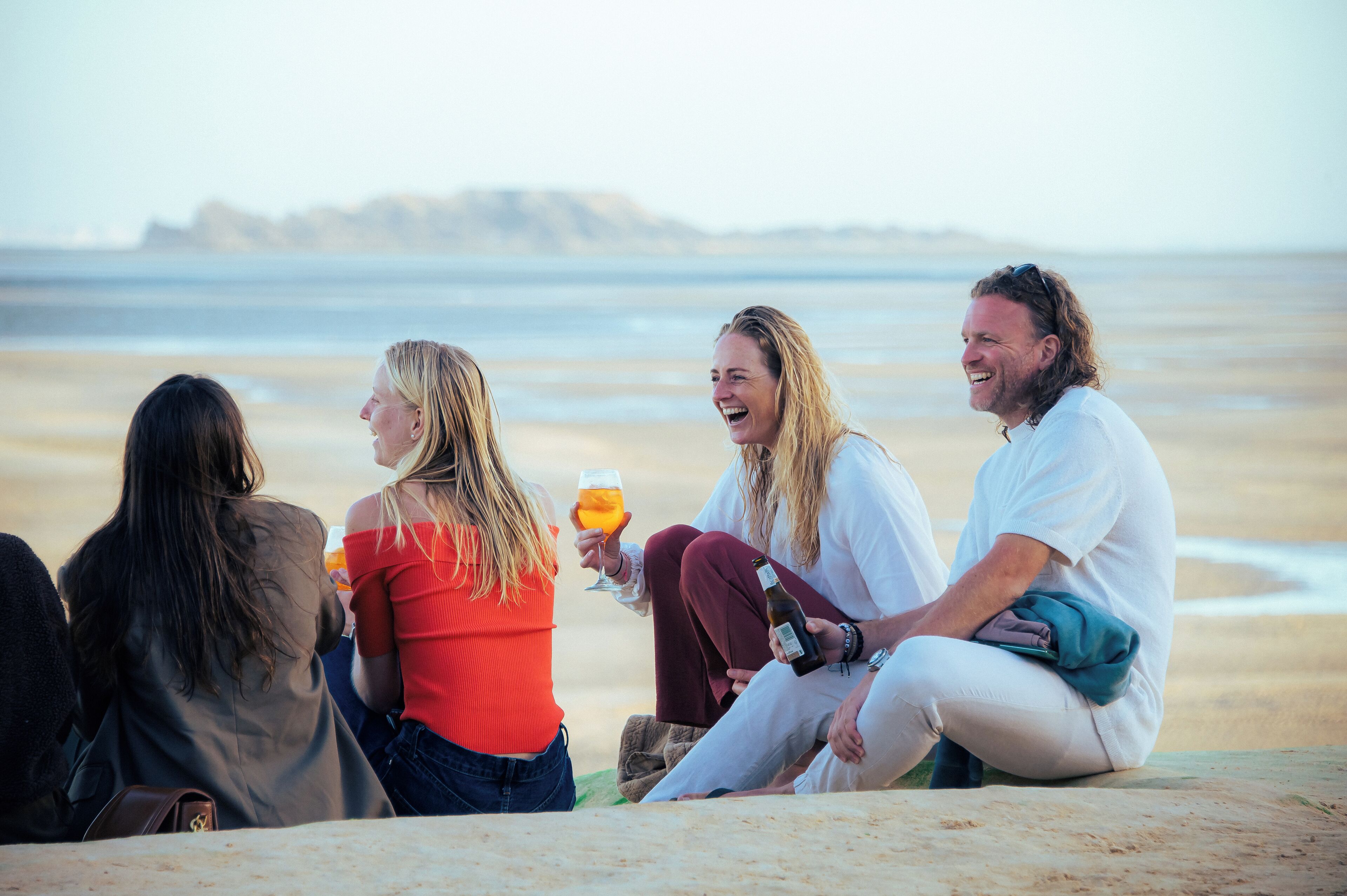 A group of people sitting on a beach with a view of the ocean and distant landforms.