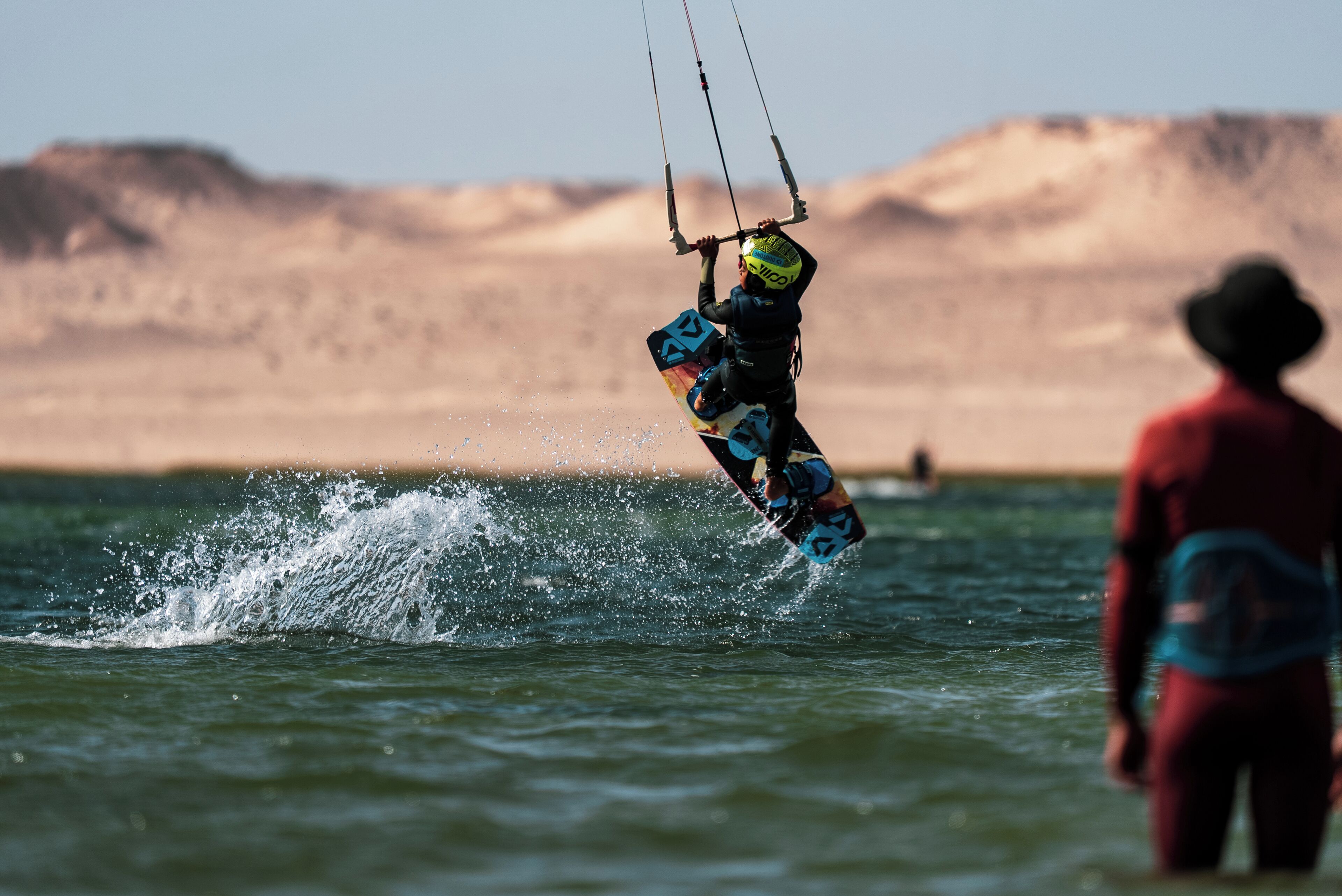 A person kiteboarding over water with a desert landscape in the background.