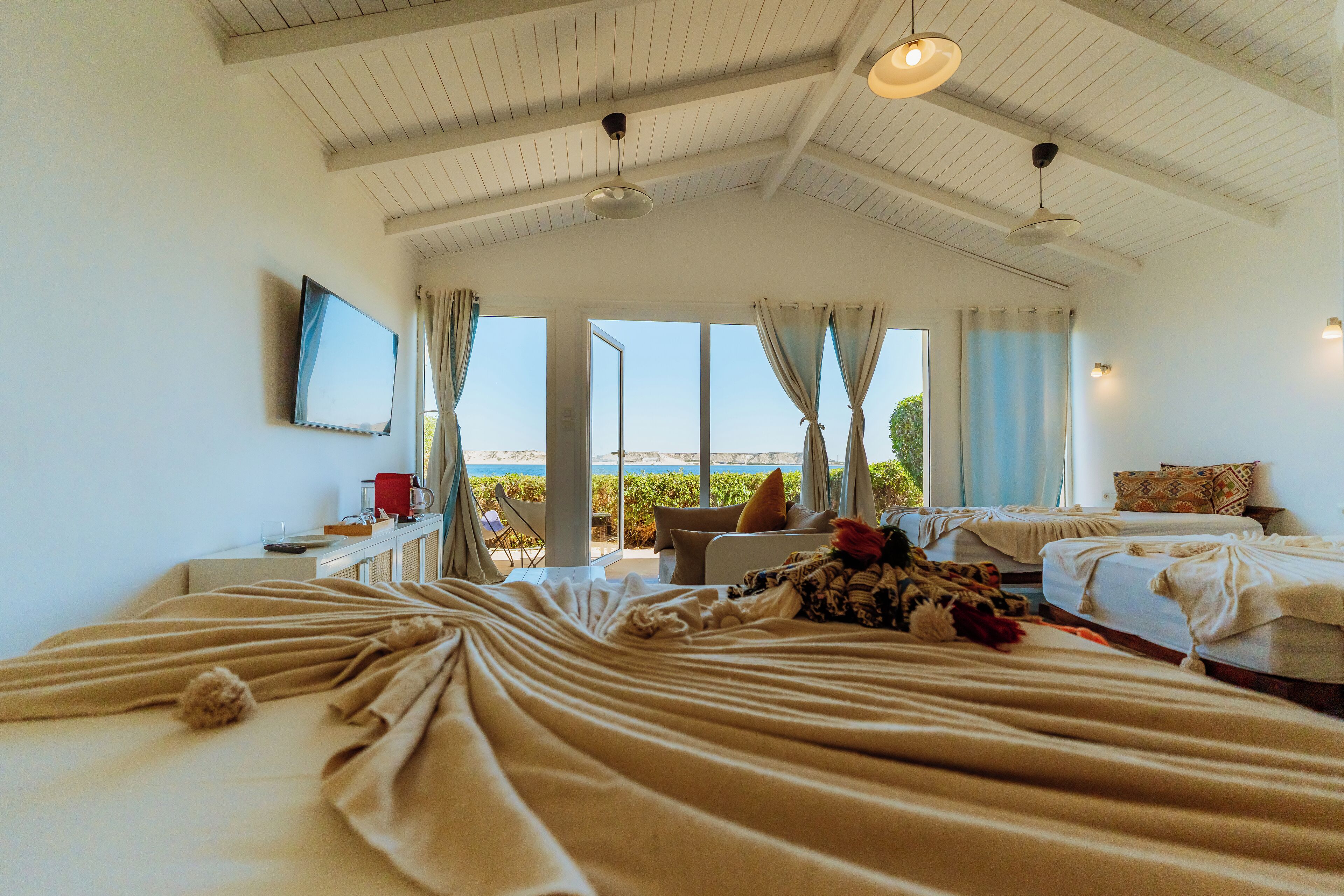 A hotel room with a large bed, a desk with a chair, a television, and a view of the sea.