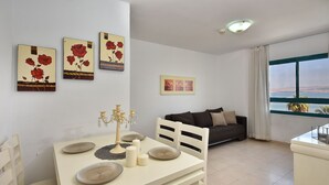 A dining area with a table set for four, a sofa, and artwork on the walls. - Family Vacation by Kinneret All Comforts (Tiberias)