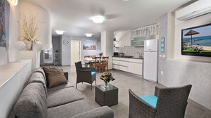 A modern living room with a grey sofa, wicker chairs, a glass coffee table, and a dining area with a table and chairs. - Luxury Suite with Jaccuzzi & Pool (Tiberias)