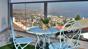 A balcony with a table and chairs, overlooking a cityscape with buildings and a body of water. - Luxury Suite with Jaccuzzi & Pool (Tiberias)