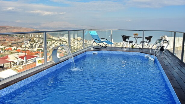 An indoor swimming pool with a clear view of the cityscape and hills in the background. - Luxury Suite with Jaccuzzi & Pool (Tiberias)