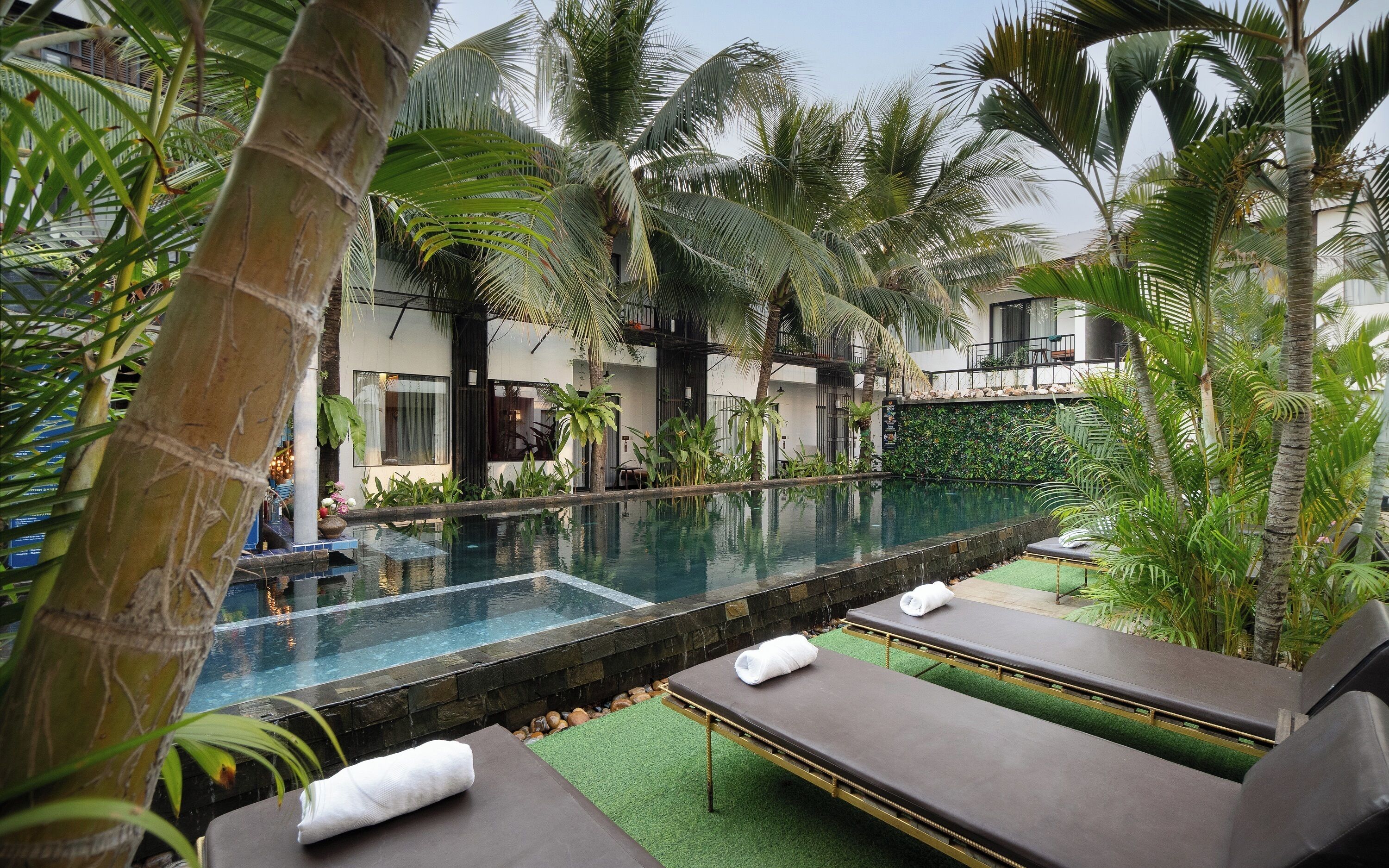 An outdoor swimming pool surrounded by palm trees and lounge chairs.