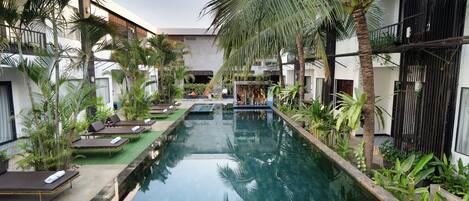 A pool area with lounge chairs and palm trees, surrounded by buildings.