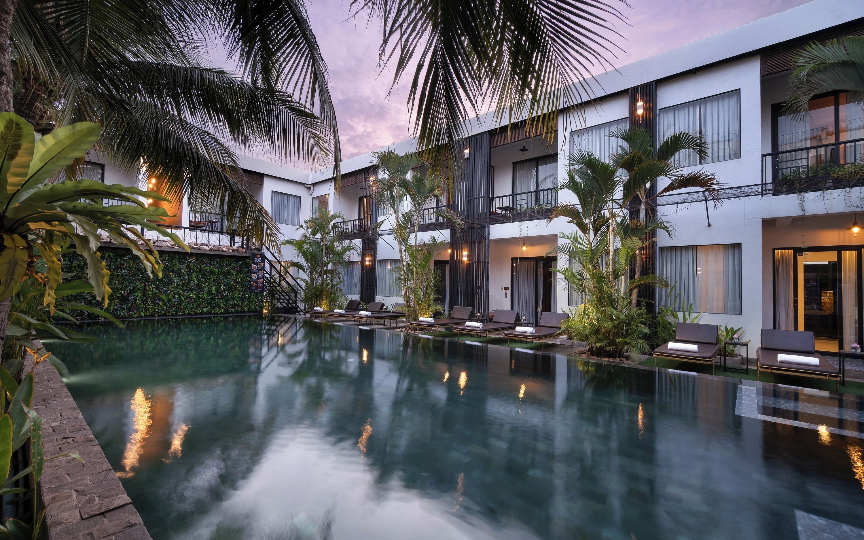 A modern hotel with a pool, palm trees, and a balcony with a view of the pool.