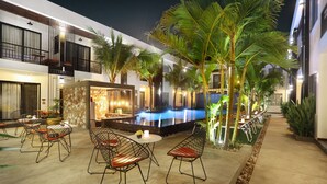 Zona de piscina exterior con mobiliario y palmeras.