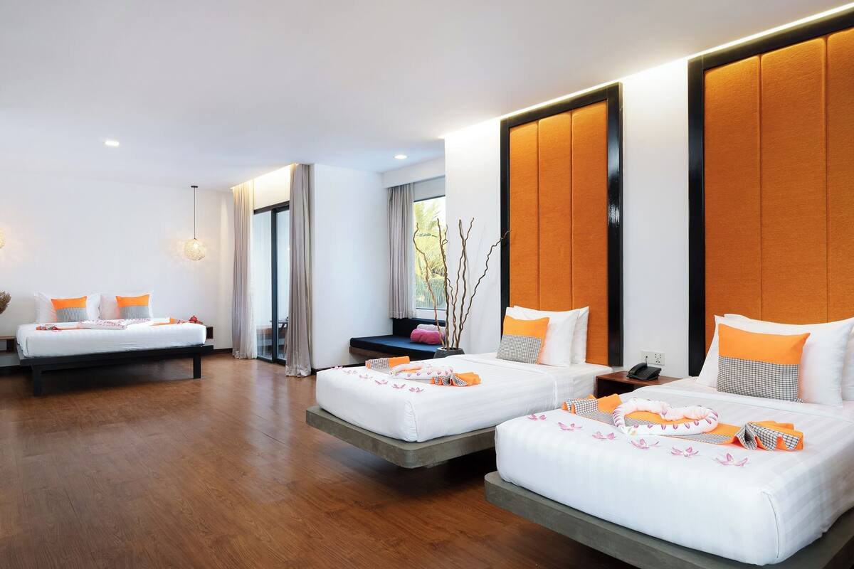A modern hotel room with two beds, a large window, and a view of greenery.