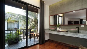 Un baño moderno con un espejo grande, un lavamanos con artículos de aseo y vistas a un balcón con plantas.
