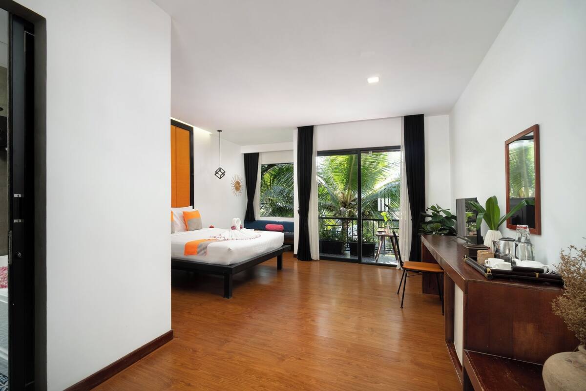 A modern hotel room with a bed, a desk, and a balcony with plants.