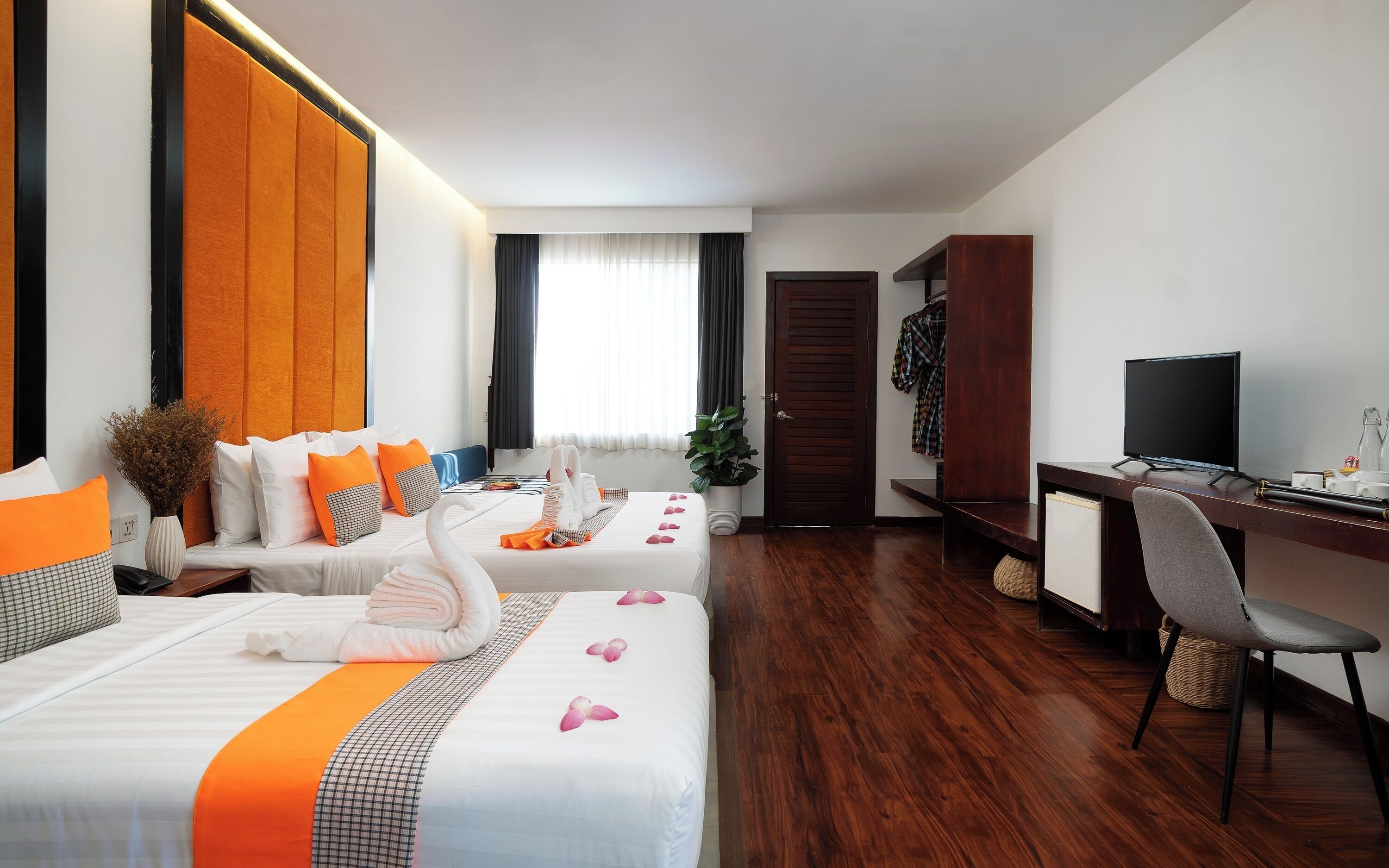 A hotel room with two beds, a desk, a TV, and a wardrobe.