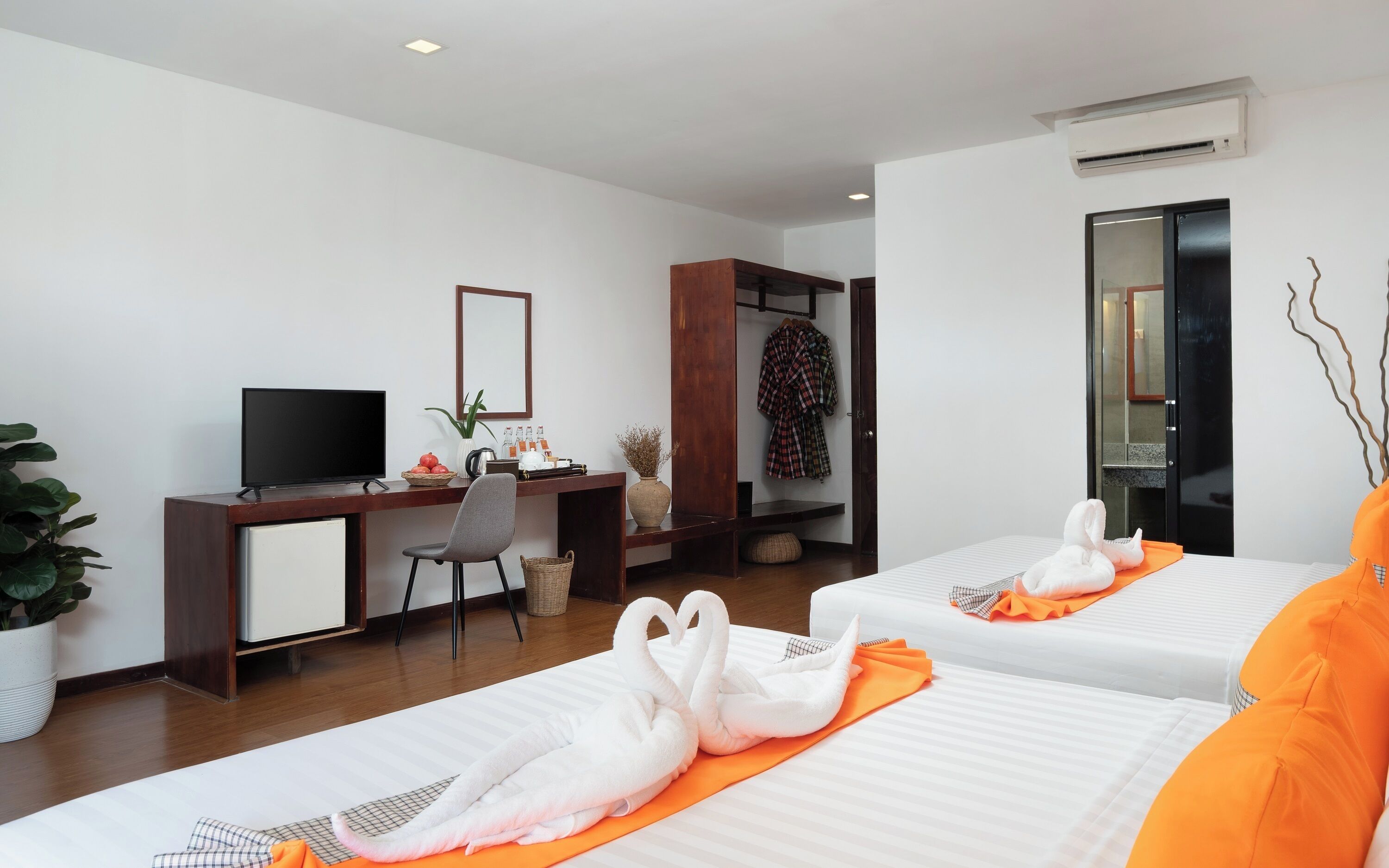 A hotel room with two beds, a desk with a TV, a wardrobe, and a potted plant.