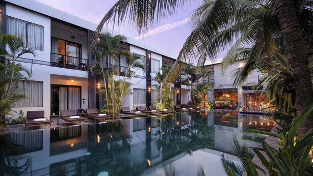 Un hotel moderno con piscina, sillas de descanso y palmeras.