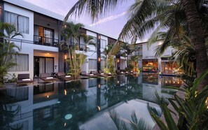 Un hotel moderno con piscina, sillas de descanso y palmeras.