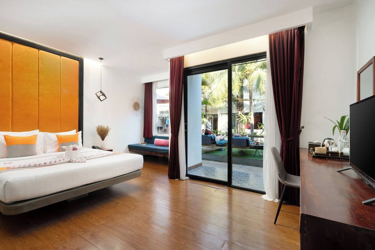 A modern hotel room with a large bed, a desk, and a view of the outdoor area.