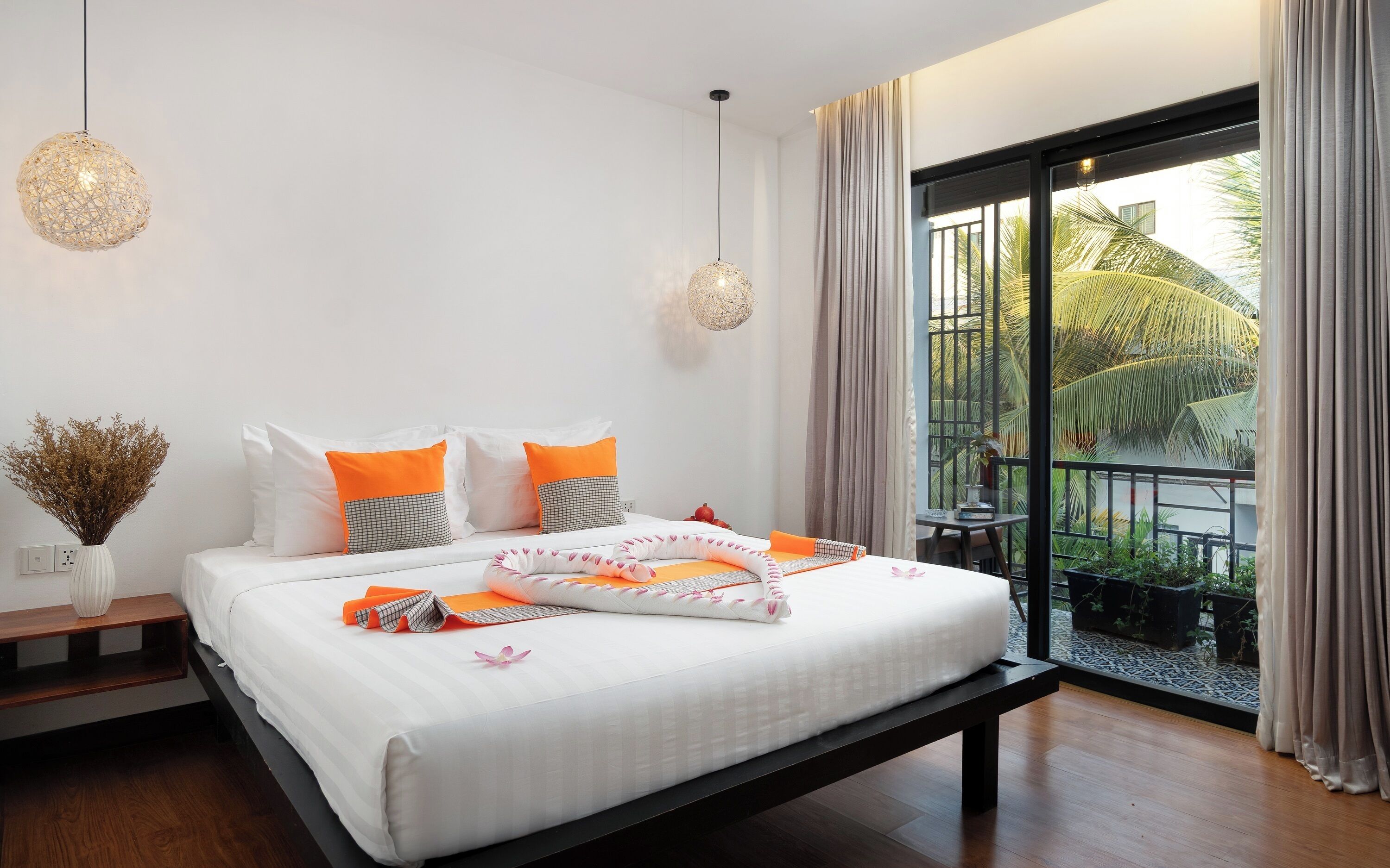 Un dormitorio moderno con cama, mesitas de noche y vistas a un balcón con plantas.