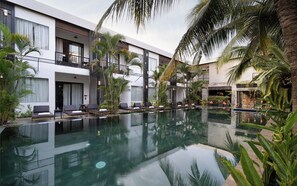 Un hotel moderno con una piscina central rodeada de sillones de descanso y palmeras.