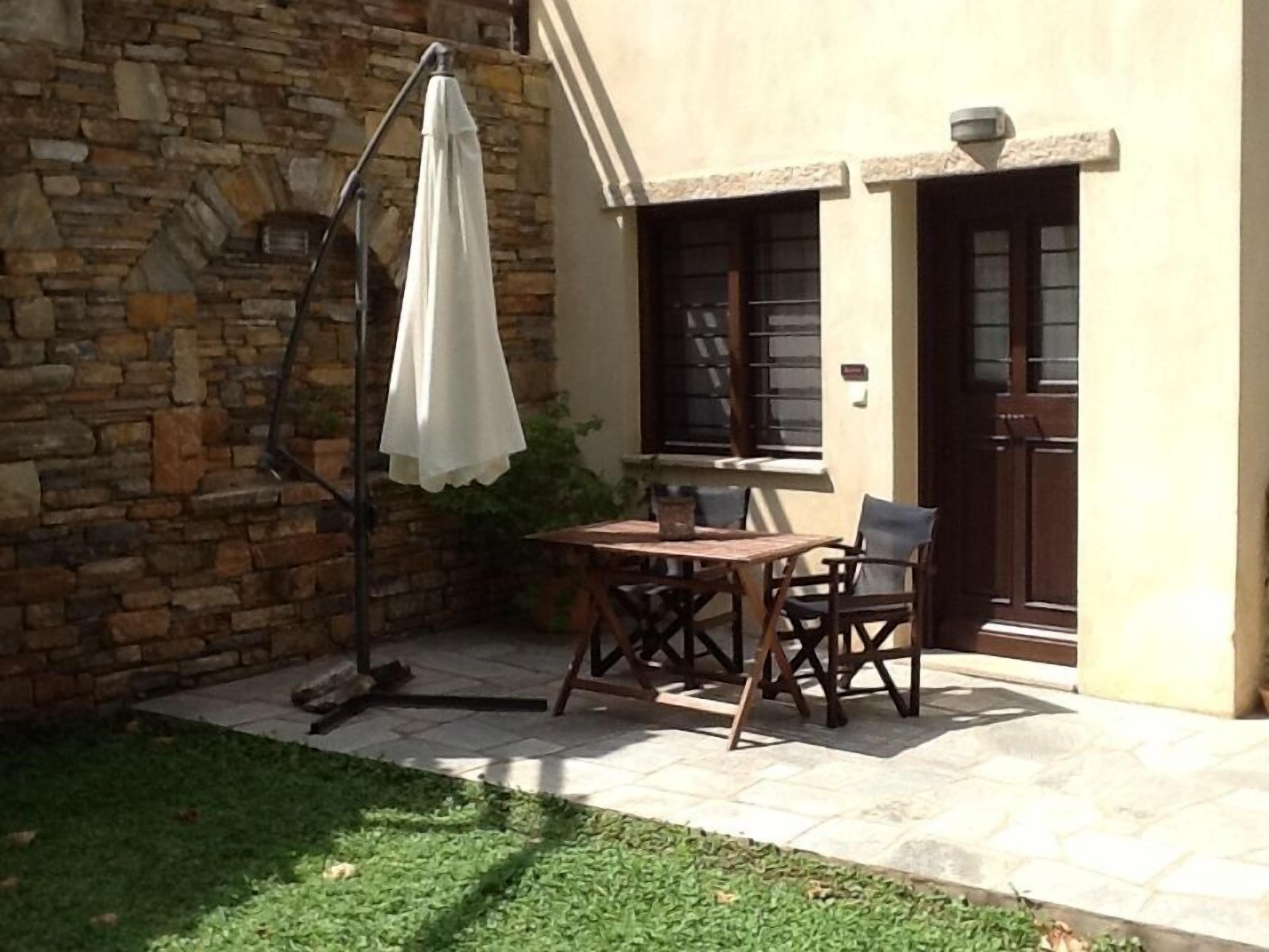 A patio with a stone wall, a table, chairs, and a white umbrella.