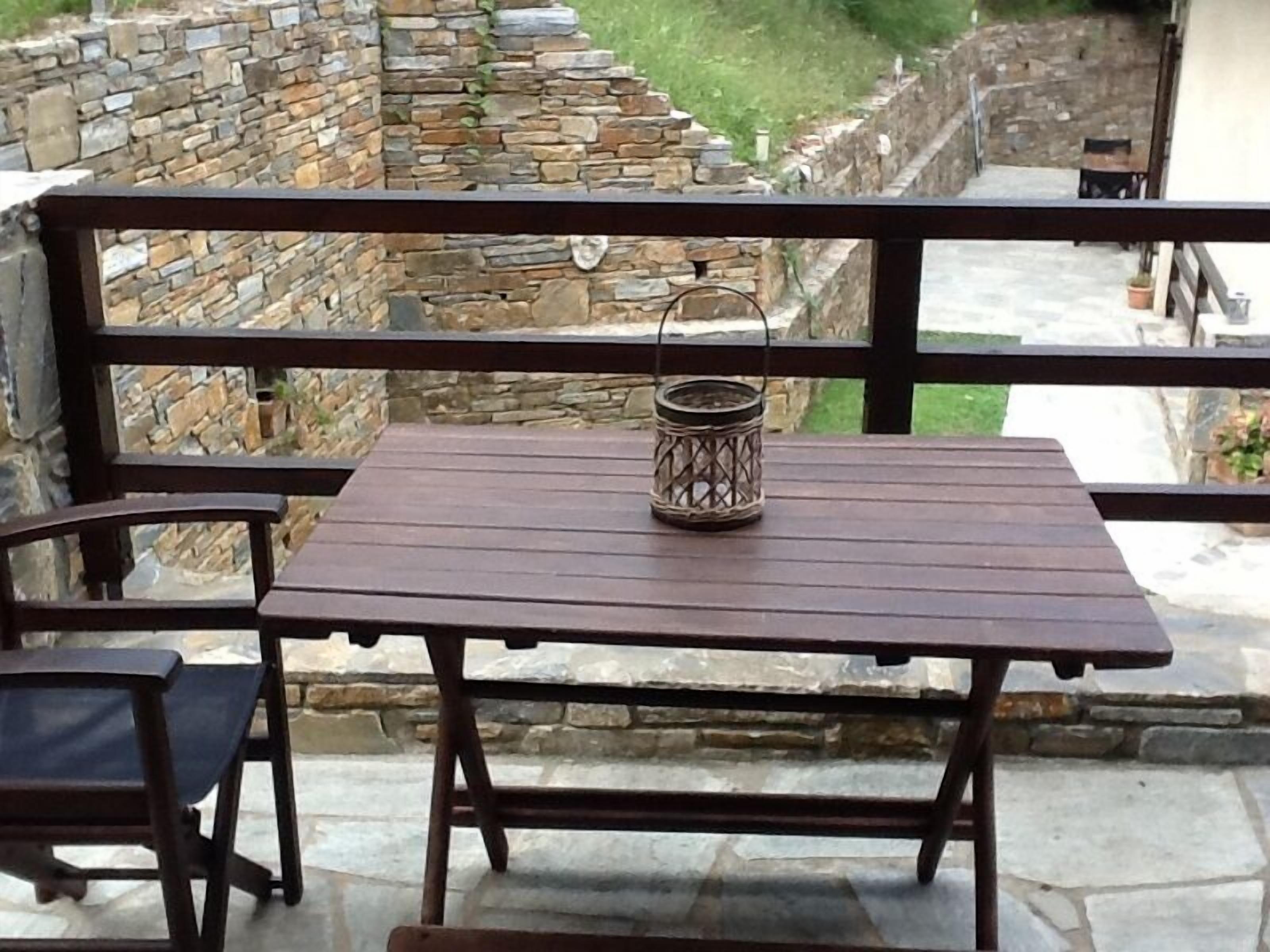 A wooden table and chairs on a balcony with stone walls in the background.